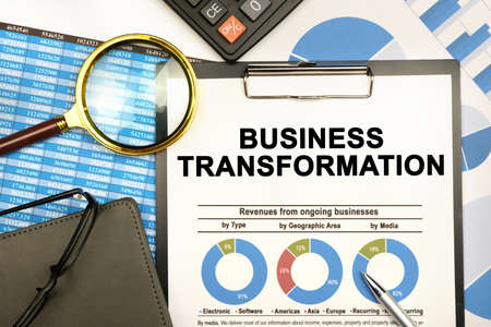 Finance and business concept. The businessman has on his desk graphs with reports, a notebook, a magnifying glass and a document with the inscription - BUSINESS TRANSFORMATIONの写真素材