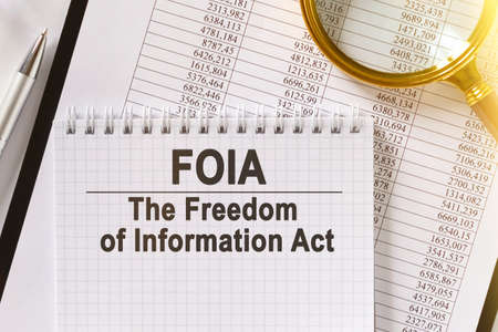 On the table are financial reports, a pen, a magnifying glass and a notebook with the inscription - FOIA. The Freedom of Information Act. Business and finance concept.の写真素材