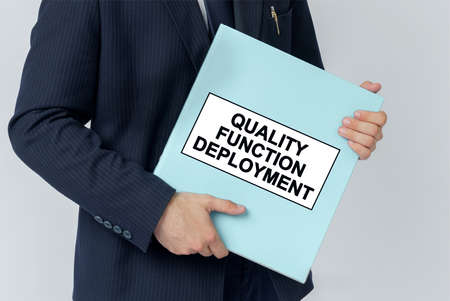Business concept. A businessman holds a folder with documents, the text on the folder is - QUALITY FUNCTION DEPLOYMENTの写真素材