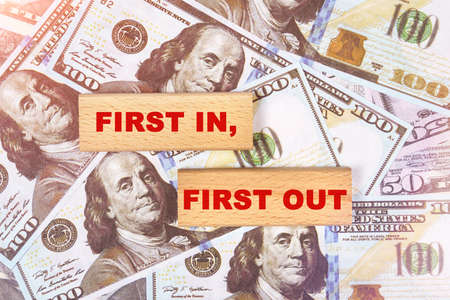 Business concept. Against the background of dollar bills, the text is written on wooden blocks - first in first outの写真素材