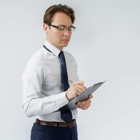 Portrait of a businessman who stands and writes down on a tablet. White background. Business and finance conceptの写真素材