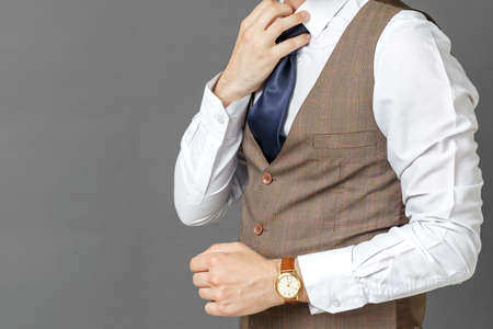 Portrait of a businessman holding his tie with his hand. The face is not visible. Gray background. Business and finance conceptの写真素材
