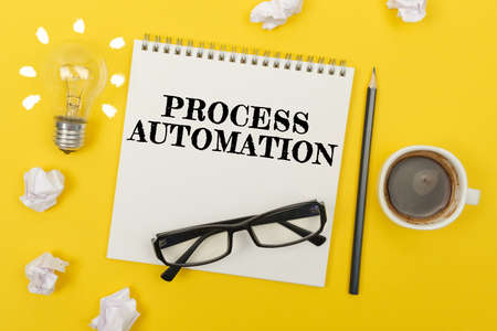 Business and finance concept. On the yellow table are: a light bulb - an idea, a cup of coffee, pieces of paper, glasses and a notebook with the inscription - PROCESS AUTOMATIONの写真素材