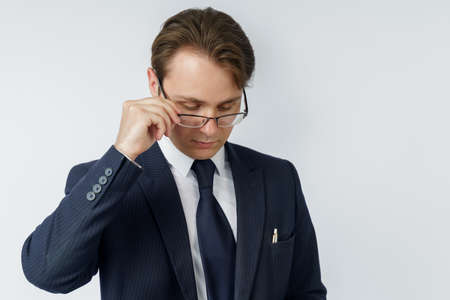 Portrait of a businessman in a blue suit, who adjusts his glasses. White background. Business and finance conceptの写真素材