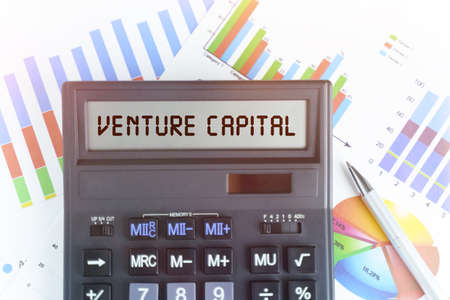 The concept of business and finance. On the table are financial charts and a calculator, on the electronic board of which is written the text - VENTURE CAPITALの写真素材