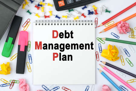 Business concept. On the table is a calculator, diary, markers, pencils and a notebook with the inscription - Debt Management Planの写真素材