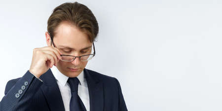 Portrait of a businessman in a blue suit, who adjusts his glasses. White background. Business and finance conceptの写真素材