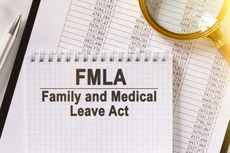 On the table are financial reports, a pen, a magnifying glass and a notebook with the inscription - FMLA. Family and Medical Leave Act. Business and finance concept.の写真素材