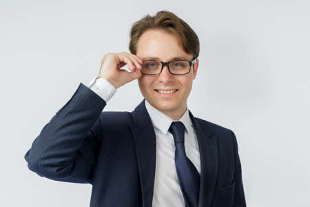 Portrait of a businessman in a blue suit, who adjusts his glasses. White background. Business and finance conceptの写真素材