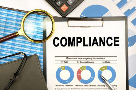 Finance and business concept. The businessman has on his desk graphs with reports, a notebook, a magnifying glass and a document with the inscription - COMPLIANCEの写真素材