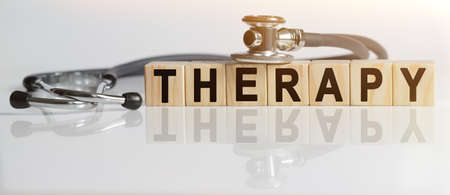THERAPY the word on wooden cubes, cubes stand on a reflective white surface, on cubes - a stethoscope. Medicine conceptの写真素材