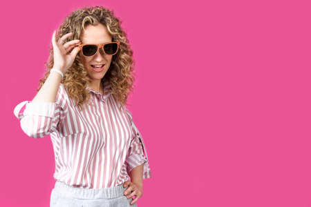 Portrait of a young, beautiful, healthy woman holding glasses and looking at the camera. Isolated on pink background.の写真素材