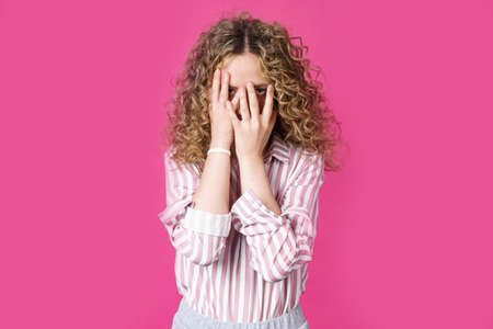 Portrait of shy, timid or ashamed pretty girl covering face and peeping through fingers, looking at camera, being curious. Body languageの写真素材