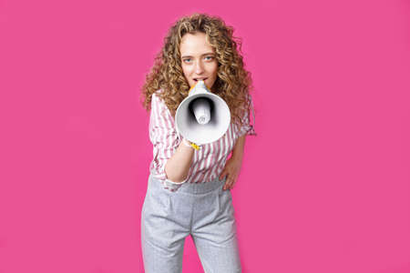 Young woman speaks into a megaphone. Isolated pink background. People sincere emotions lifestyle concept.の写真素材