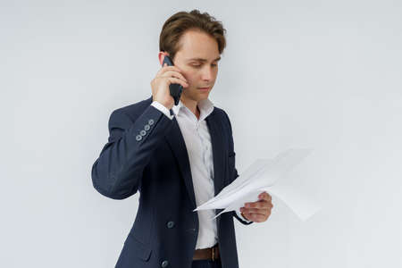 Portrait of a businessman who is talking on the phone and reading documents. White background.の写真素材