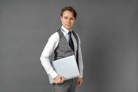 Portrait of a businessman who holds a laptop in his hands. Gray background. Business and finance conceptの写真素材