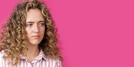 A side shot of a beautiful upset woman with curly hair holding her arms folded. Isolated on pink background.の写真素材