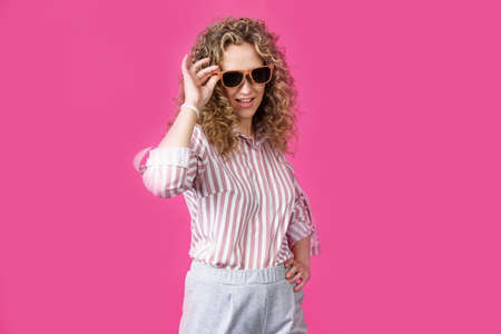 Portrait of a young, beautiful, healthy woman holding glasses and looking at the camera. Isolated on pink background.の写真素材