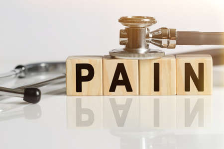 PAIN the word on wooden cubes, cubes stand on a reflective white surface, on cubes - a stethoscope. Medicine conceptの写真素材