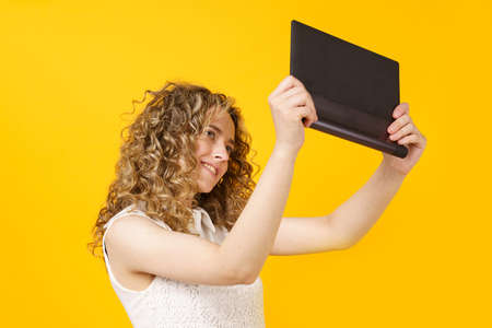 Portrait of a young woman who communicates on a tablet. Female portrait. Isolated on yellow backgroundの写真素材