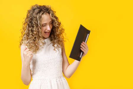 Portrait of a young woman who emotionally rejoices at success after reading information on a tablet. Female portrait. Isolated on yellow backgroundの写真素材