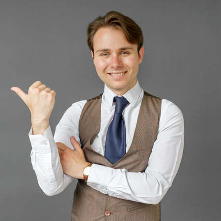 An emotional portrait of a businessman who shows a gesture of his hand to the right. Gray background. Business and finance conceptの写真素材