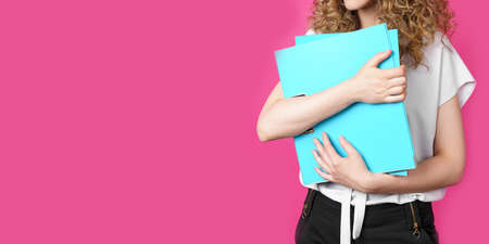 A young woman holds folders with documents in her hands. Isolated on pink background