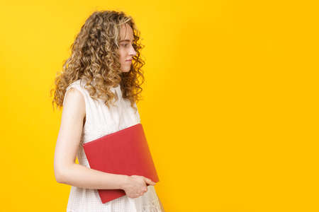 Portrait of a young smiling woman who holds a book in her hands. Female portrait. Isolated on yellow...