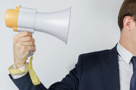 A businessman is holding a loudspeaker that is directed towards his face. White background. Business and finance conceptの写真素材