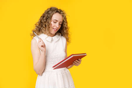 A young woman holds a textbook and a pen. Female portrait. Isolated on yellow background