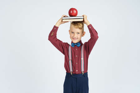 A schoolboy holds books with an apple on his head, smiles. Isolated background. Education conceptの写真素材