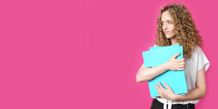 A young woman holds folders with documents in her hands. Isolated on pink background