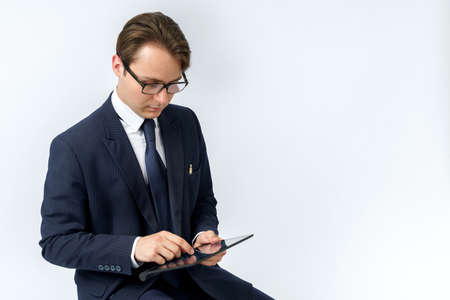 Portrait of a businessman in a blue suit who sits and works with an electronic tablet. White background. Business and finance conceptの写真素材