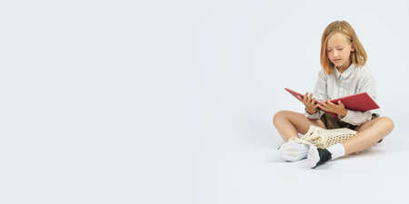 Teenage girl sitting on the floor and reading a book. Isolated background. Education concept.