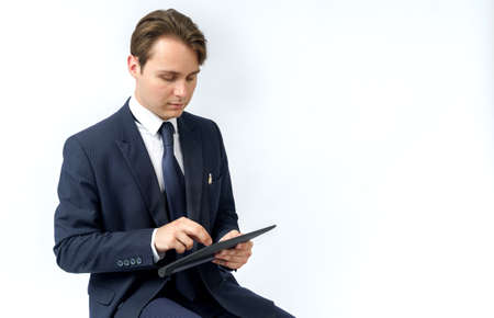 Portrait of a businessman in a blue suit who sits and works with an electronic tablet. White...