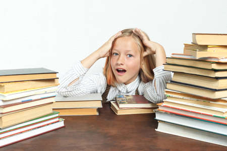 Portrait of a teenage girl sitting at a table tired among the books and doing her homework. Holds...