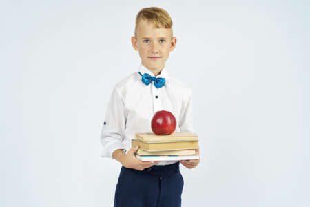 The schoolboy holds books and an apple in his hands. Isolated background. Education conceptの写真素材