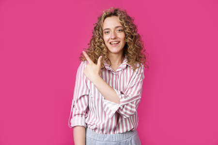 Young beautiful woman shows her finger to the left. Isolated pink backgroundの写真素材