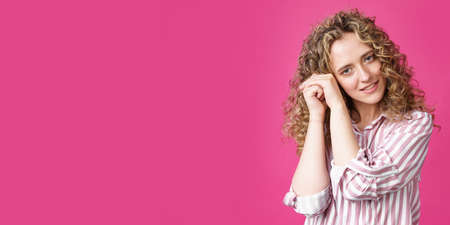 Happy contented woman holds her hands together near the face. Isolated on pink backgroundの写真素材
