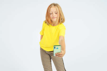A teenage girl in a yellow T-shirt takes a selfie on a mobile phone. Isolated background. Education...