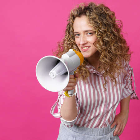 Young woman speaks into a megaphone. Isolated pink background. People sincere emotions lifestyle concept.の写真素材
