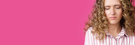 A side shot of a beautiful upset woman with curly hair holding her arms folded. Isolated on pink background.の写真素材