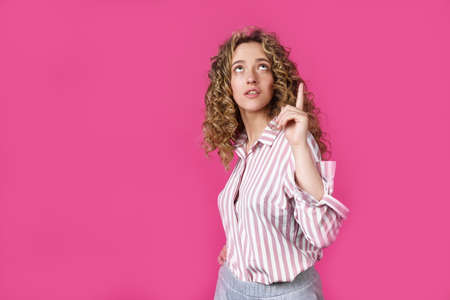 Young beautiful woman, amazed and surprised, looking up and pointing with fingers and raised hands....