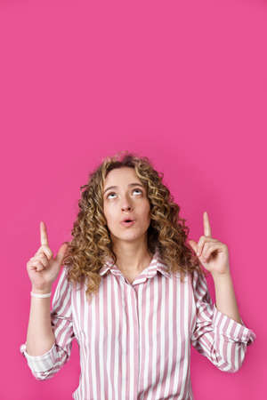 Young beautiful woman, amazed and surprised, looking up and pointing with fingers and raised hands....
