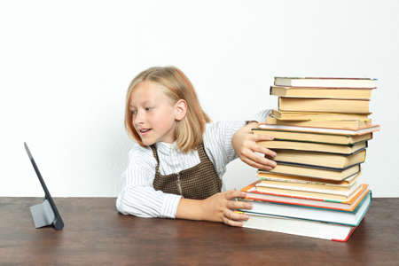 Education concept. Teenage girl pushes books aside, choosing a tablet for learning.