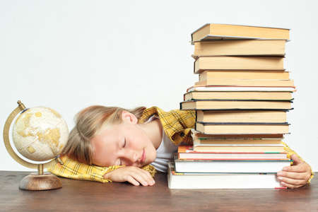 Education concept. Teenage girl fell asleep doing homework. Next to the student on the table are books and a globe.の写真素材