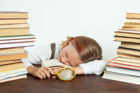 Education concept. A teenage girl with a magnifying glass in her hands fell asleep among the books.の写真素材