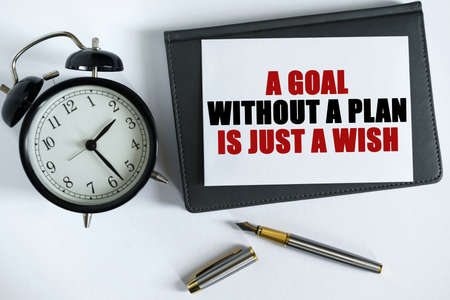 Business and positive concept. On the table there is a clock, a pen, a notebook and a card on which the text is written - A GOAL WITHOUT A PLAN IS JUST A WISH.の写真素材