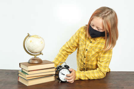 Education concept. A girl in a mask stands near the table. There is a globe on the table, books and...