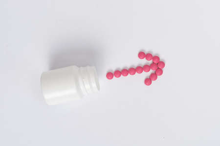 Medicine concept. On a white background lies a white jar and pink pills laid out in the form of an...